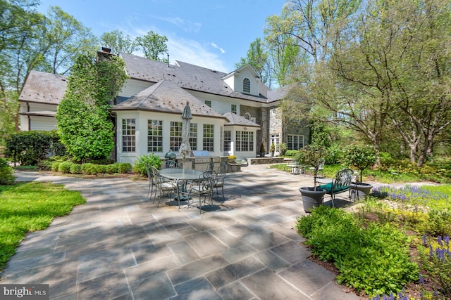 back of property featuring a high end roof, stone siding, a chimney, and a patio area