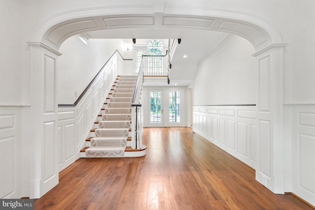 stairs featuring arched walkways, hardwood / wood-style flooring, wainscoting, and a decorative wall