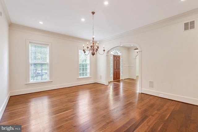 unfurnished dining area featuring wood finished floors, arched walkways, visible vents, and a chandelier