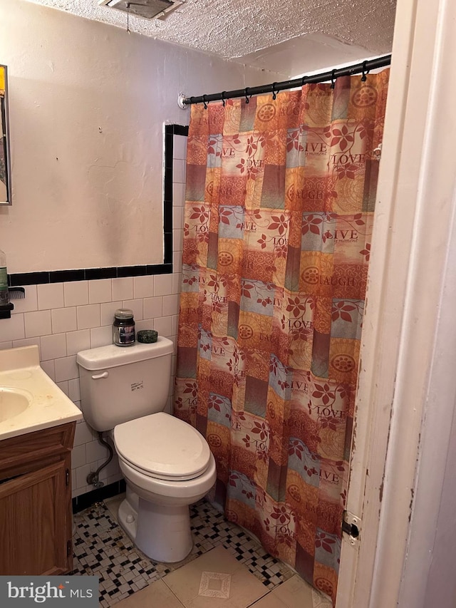 full bath featuring toilet, a textured ceiling, tile walls, tile patterned flooring, and vanity