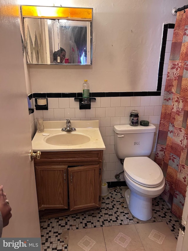 bathroom featuring toilet, a shower with shower curtain, vanity, wainscoting, and tile walls