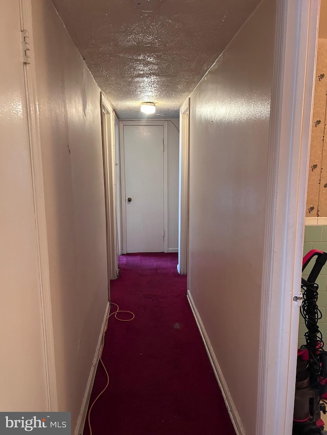 hall featuring baseboards, a textured ceiling, and carpet