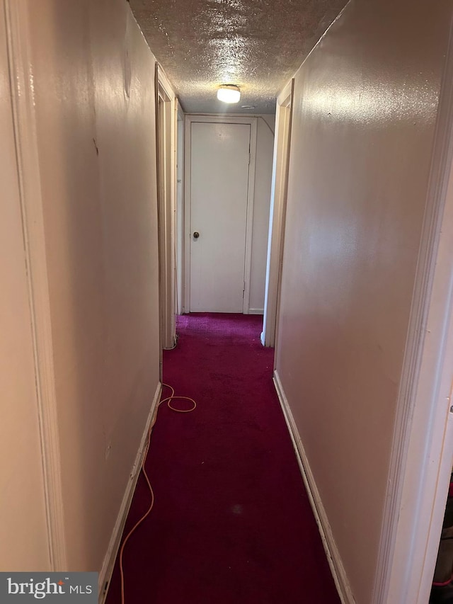 corridor with baseboards, dark colored carpet, and a textured ceiling