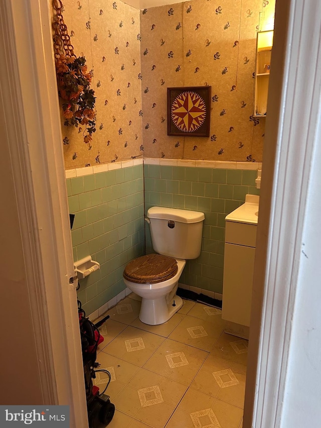 half bathroom with tile patterned flooring, wainscoting, wallpapered walls, and toilet