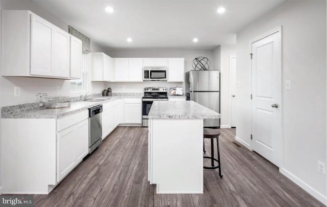 kitchen with a kitchen island, a breakfast bar area, stainless steel appliances, dark wood-style floors, and white cabinetry