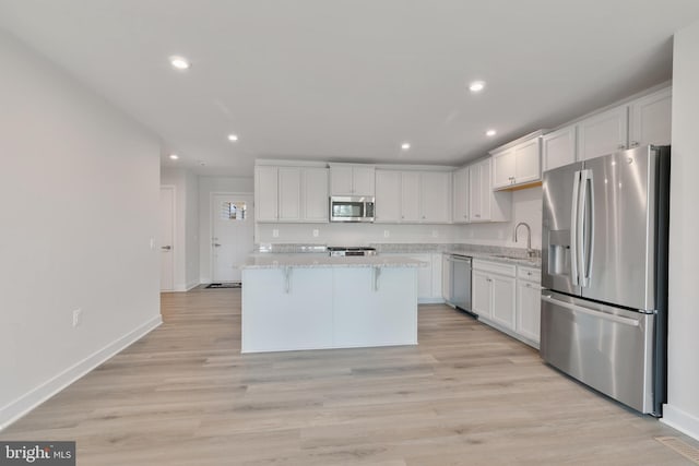 kitchen featuring white cabinets, appliances with stainless steel finishes, light wood-style floors, and a sink