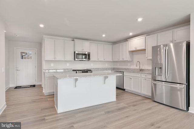 kitchen with a kitchen bar, a sink, a center island, appliances with stainless steel finishes, and light wood finished floors