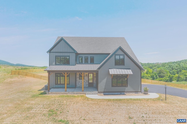 modern farmhouse style home featuring board and batten siding, fence, roof with shingles, a front yard, and metal roof