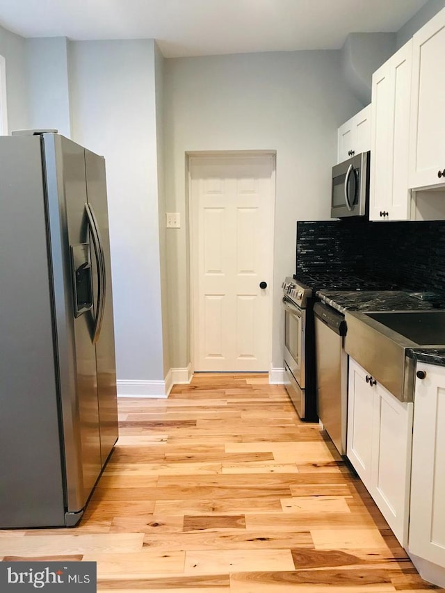 kitchen with light wood-style flooring, dark countertops, white cabinetry, appliances with stainless steel finishes, and baseboards