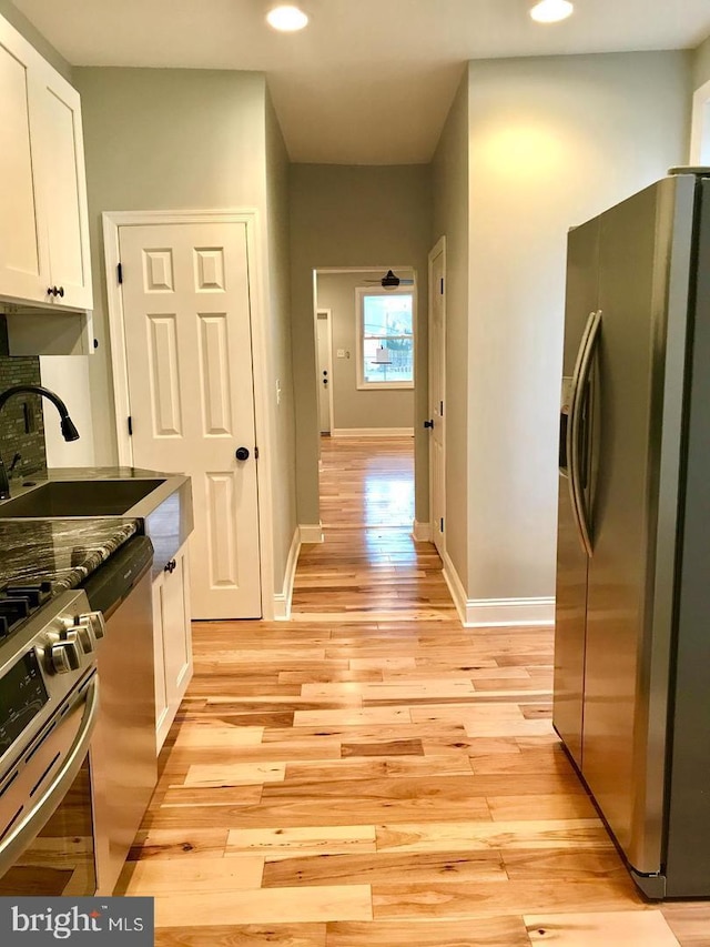 kitchen with light wood-style flooring, a sink, white cabinetry, appliances with stainless steel finishes, and baseboards