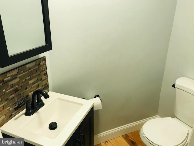 half bath with vanity, wood finished floors, baseboards, toilet, and tasteful backsplash