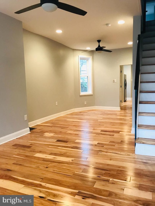 unfurnished living room featuring stairway, baseboards, light wood-style floors, and a ceiling fan