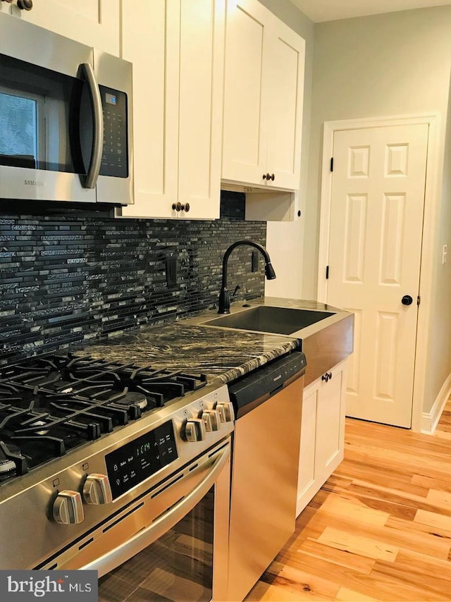 kitchen featuring a sink, stainless steel appliances, white cabinetry, light wood-type flooring, and backsplash