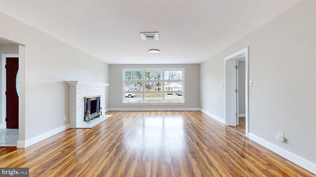 unfurnished living room featuring a brick fireplace, baseboards, and wood finished floors