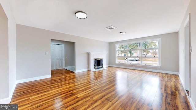 unfurnished living room with visible vents, baseboards, a brick fireplace, and wood finished floors