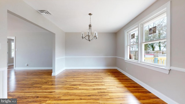 unfurnished room with light wood-style floors, visible vents, baseboards, and a notable chandelier