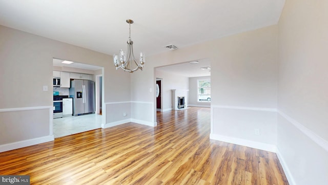 unfurnished room featuring light wood-style flooring, baseboards, visible vents, and a chandelier