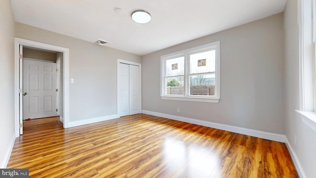 unfurnished bedroom with light wood-type flooring, baseboards, a closet, and visible vents