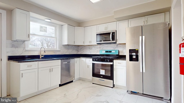 kitchen with a sink, stainless steel appliances, white cabinets, dark countertops, and marble finish floor