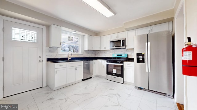 kitchen with a sink, decorative backsplash, appliances with stainless steel finishes, dark countertops, and marble finish floor