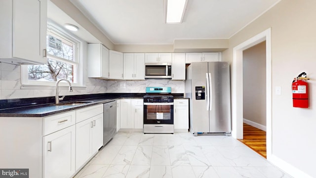 kitchen with dark countertops, backsplash, marble finish floor, stainless steel appliances, and a sink