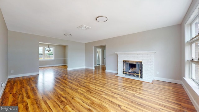 unfurnished living room with baseboards, light wood-style floors, an inviting chandelier, and a fireplace