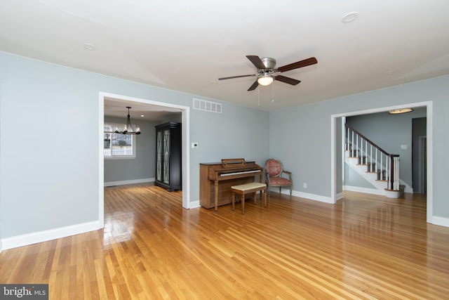 living area with visible vents, light wood-style flooring, ceiling fan with notable chandelier, stairway, and baseboards