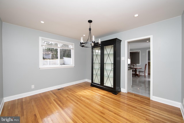 spare room with light wood finished floors, visible vents, baseboards, and an inviting chandelier