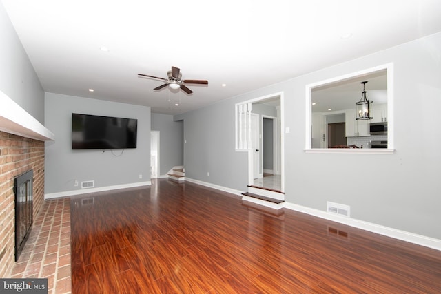 unfurnished living room featuring visible vents, a brick fireplace, baseboards, wood finished floors, and a ceiling fan