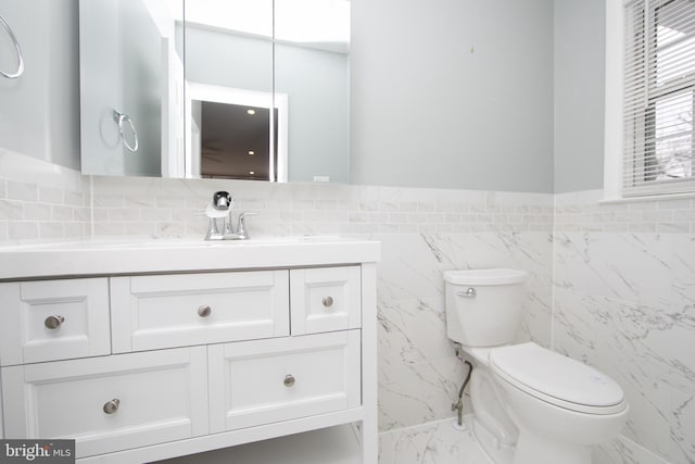 bathroom with tile walls, marble finish floor, toilet, and vanity