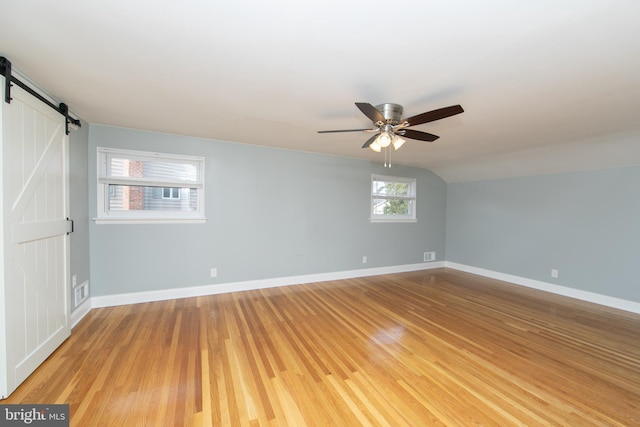 unfurnished room with visible vents, ceiling fan, baseboards, a barn door, and light wood-style floors