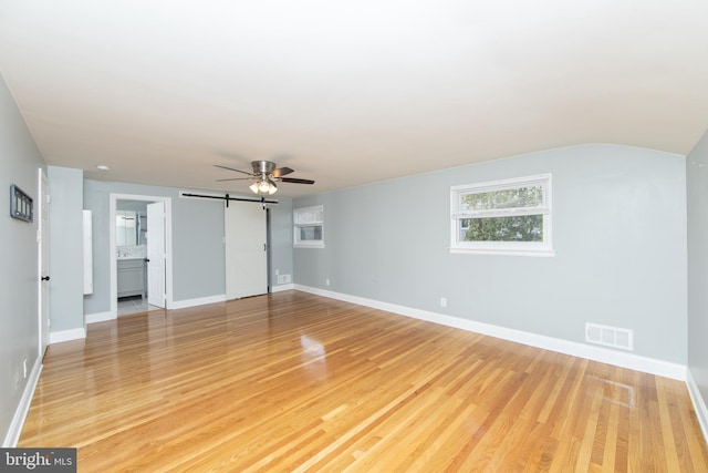 unfurnished living room with visible vents, ceiling fan, baseboards, a barn door, and light wood-style floors