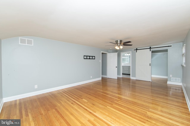 unfurnished living room featuring baseboards, visible vents, light wood finished floors, ceiling fan, and a barn door