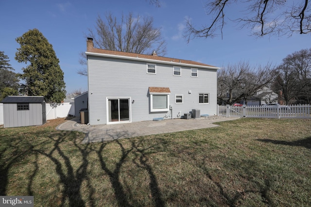 back of property featuring a shed, a chimney, a yard, a fenced backyard, and an outbuilding