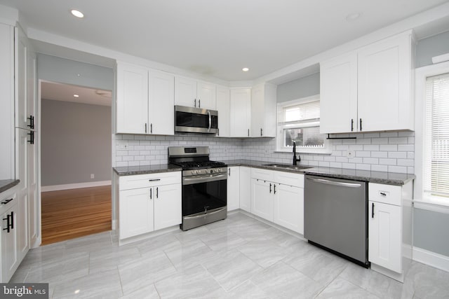 kitchen with white cabinetry, appliances with stainless steel finishes, dark stone counters, and a sink