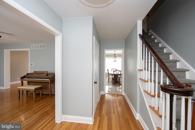 corridor featuring baseboards, visible vents, light wood finished floors, stairs, and a chandelier