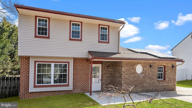 traditional home featuring roof mounted solar panels, brick siding, and fence