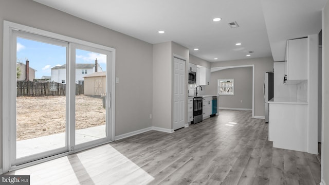 unfurnished living room with light wood finished floors, recessed lighting, baseboards, and a wealth of natural light