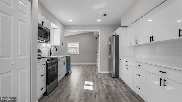 kitchen featuring light wood-type flooring, light countertops, appliances with stainless steel finishes, white cabinetry, and a sink