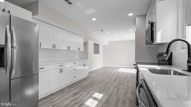 kitchen with backsplash, recessed lighting, stainless steel appliances, light wood-style floors, and white cabinetry