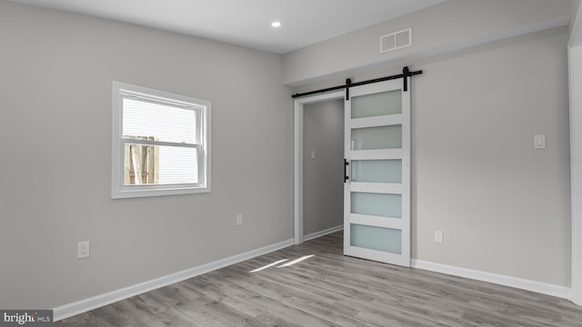 unfurnished bedroom with visible vents, wood finished floors, recessed lighting, a barn door, and baseboards