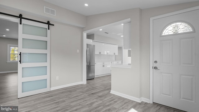 entrance foyer featuring a barn door, baseboards, visible vents, and light wood-type flooring