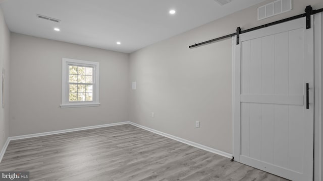 empty room with recessed lighting, visible vents, light wood-style flooring, and a barn door