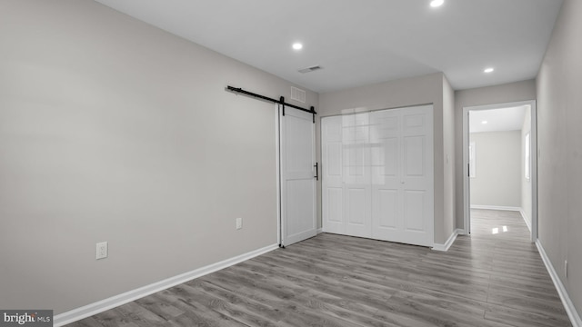 unfurnished bedroom featuring recessed lighting, a barn door, baseboards, and wood finished floors