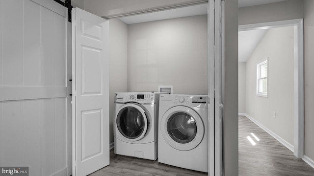 washroom with washer and clothes dryer, wood finished floors, a barn door, baseboards, and laundry area