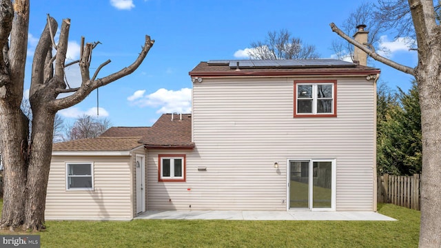 rear view of property featuring a patio, a lawn, solar panels, and fence