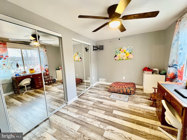 bedroom featuring a ceiling fan, baseboards, light wood finished floors, visible vents, and two closets