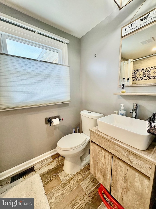 bathroom with wood finished floors, toilet, baseboards, and visible vents