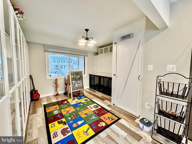 recreation room featuring a notable chandelier, light wood-style flooring, a fireplace, and baseboards