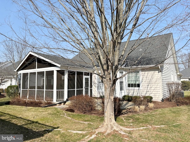 back of house featuring a lawn, roof with shingles, and a sunroom